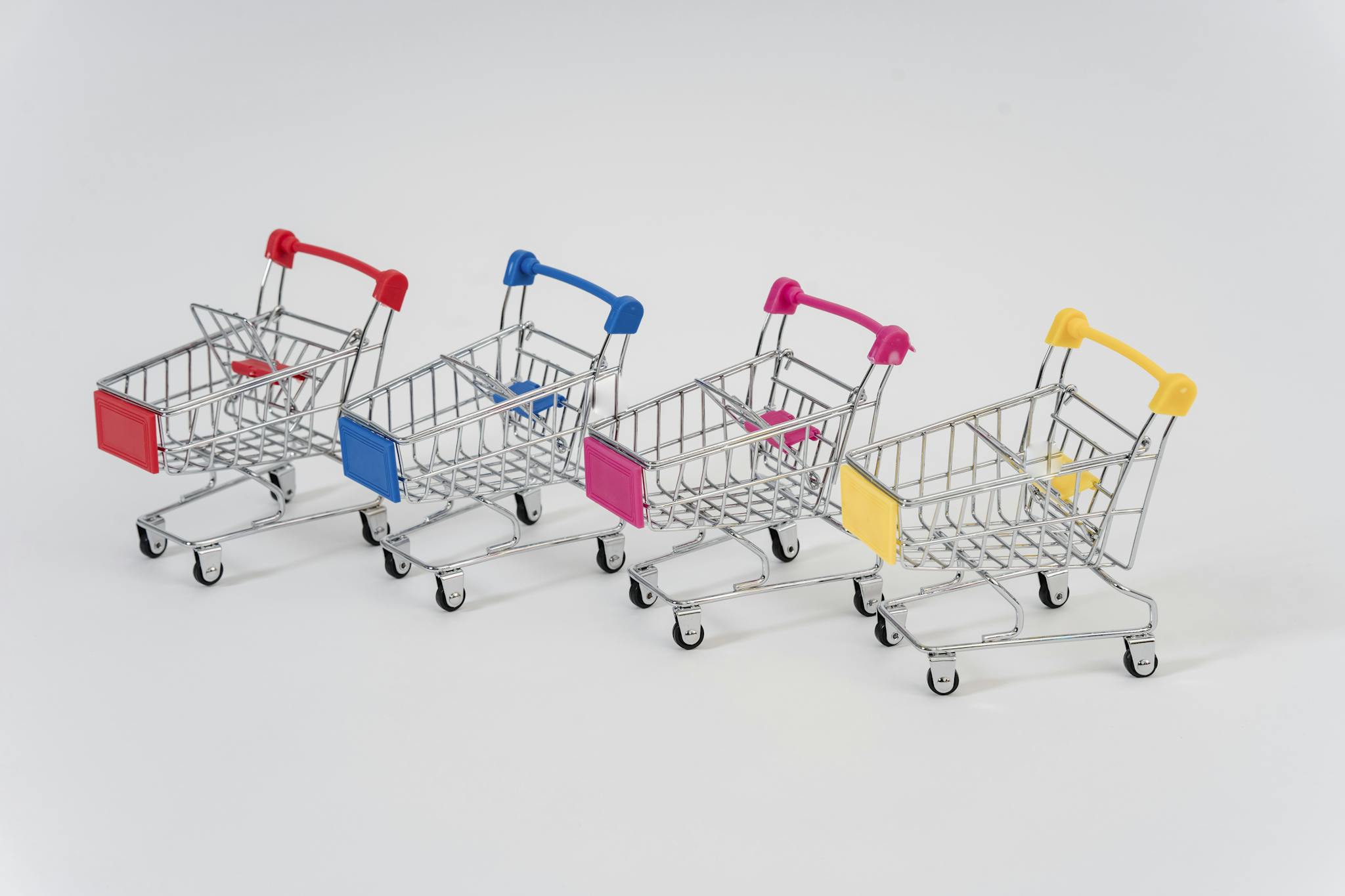 Four miniature shopping carts with colorful handles aligned on a white background for conceptual business imagery.